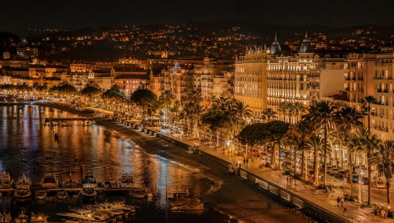 La Croisette in Cannes at night, illuminated palm trees and palace façades.